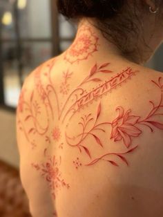 the back of a woman's shoulder with red flowers on it and writing in cursive ink