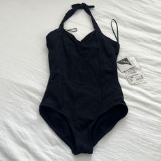 a black swimsuit laying on top of a bed next to a tag and some papers