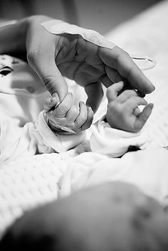 a black and white photo of two hands on a baby's hand while holding an object in the other hand