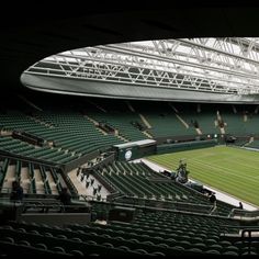 an empty tennis stadium filled with lots of green seats and people standing on the sidelines