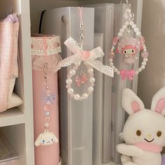 a white stuffed animal sitting next to a pink pen and keychain on a shelf