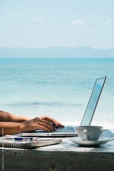 a woman sitting at a table with a laptop computer on her lap by the ocean