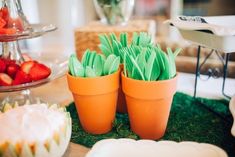 there are two orange pots with green flowers in them and strawberries on the table