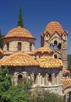 an old building with orange tiled roofs and trees in the foreground on a sunny day