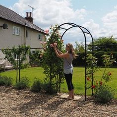 a woman standing in front of a house next to a garden with roses on it