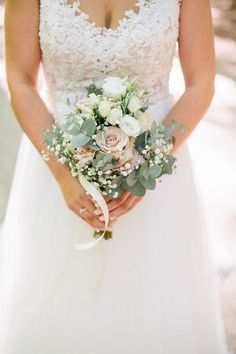 a woman in a wedding dress holding a bridal bouquet with greenery and flowers