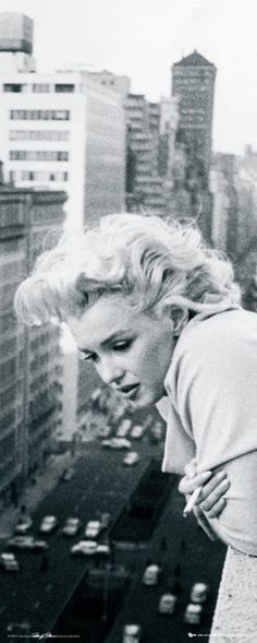 a black and white photo of a woman leaning on a ledge with buildings in the background