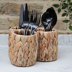 black plastic forks and spoons are in a woven basket on a marble countertop