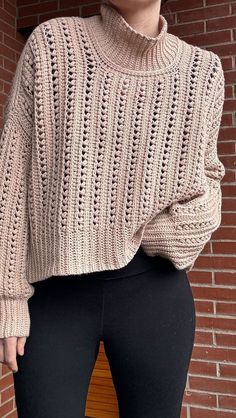 a woman wearing black leggings and a beige sweater standing in front of a brick wall