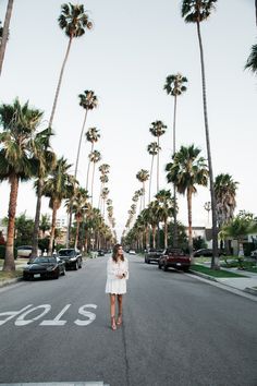 a woman standing in the middle of an empty street with palm trees on both sides