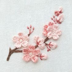 pink crocheted flowers are displayed on a white fabric background with brown stems and leaves