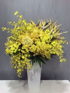 a white vase filled with yellow flowers sitting on top of a table next to a gray wall