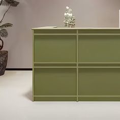 a green cabinet sitting on top of a white floor next to a potted plant