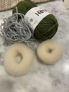 two balls of yarn sitting on top of a table next to donuts and knitting needles