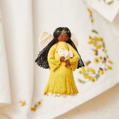 an angel ornament hanging from a string on a white table with yellow flowers