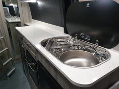 a stainless steel sink in a kitchen with black cabinets and white counter tops, next to an oven