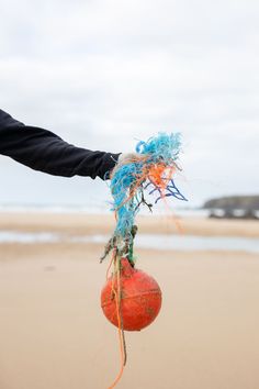 a person holding an object on the beach with blue and orange string attached to it