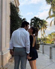 a man and woman standing next to each other on a sidewalk with palm trees in the background