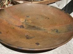 an old brown plate sitting on top of a cement floor next to a wooden bowl