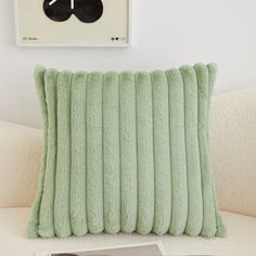 a green pillow sitting on top of a white couch next to a framed photograph and clock