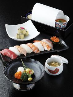 sushi is served on black plates with chopsticks