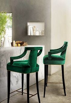 two green chairs sitting next to each other in front of a counter with vases on it