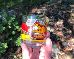 someone holding up a glass with garfield the cat on it in front of some bushes