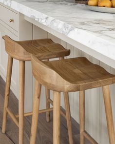 two wooden stools sitting on top of a counter next to a bowl of fruit