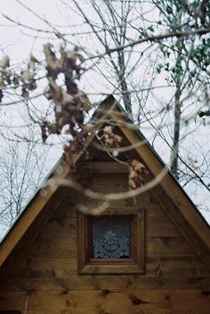 the roof of a small wooden cabin with a window in it's center surrounded by trees