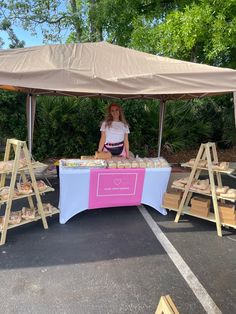 a woman standing behind a table with food on it in front of a large tent