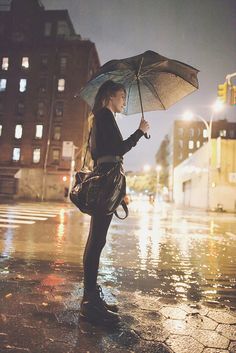 a woman standing in the rain holding an umbrella