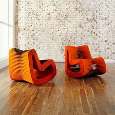 two orange chairs sitting on top of a hard wood floor next to a white brick wall