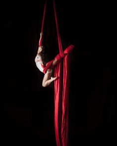 a woman is doing aerial acrobatic tricks on a red rope in the dark