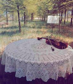 an old violin sits on top of a table in the woods, with a crocheted doily covering it