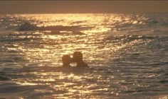 two people are swimming in the ocean at sunset or sunrise with their backs to each other