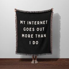 a woman standing in front of a wall holding a black blanket that says, my internet goes out more than i do