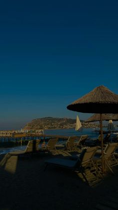 lounge chairs and umbrellas are on the beach by the water with buildings in the background