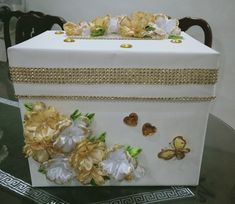 a white box with gold trim and flowers on the side sitting on a glass table