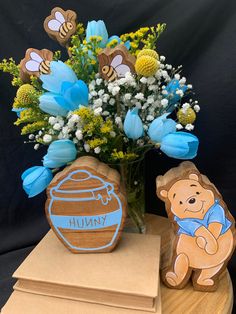 a vase filled with blue flowers next to a winnie the pooh cookie on top of a wooden stand