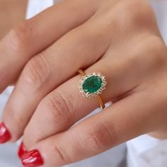 a woman's hand wearing a ring with an oval emerald and diamond halo setting