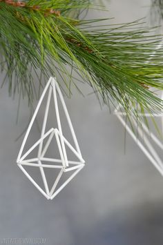 a white ornament hanging from a pine tree with the shape of a diamond on it