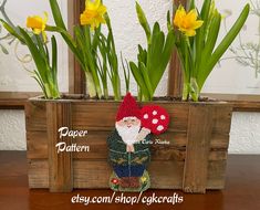 a crocheted gnome is sitting in front of some yellow flowers and green leaves