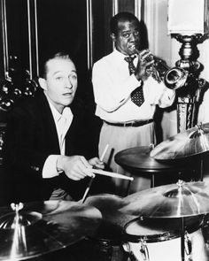 two men are playing drums in a black and white photo, one is holding a trumpet