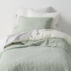 an unmade bed with green and white comforter on the bottom, along with two pillows