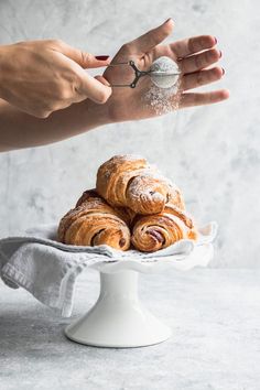 a person reaching out their hand to grab some pastries from a white cake plate