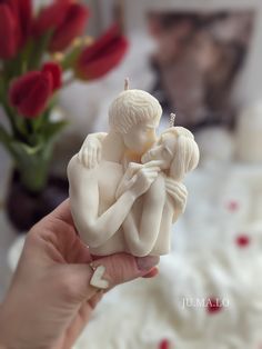 a person holding a small white figurine in front of a vase with red flowers