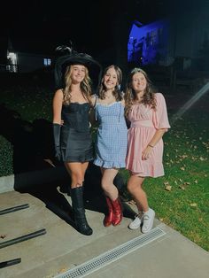 three young women standing next to each other in front of a house at night time