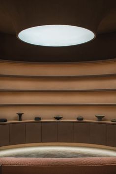 an empty room with several vases and bowls on the wall, in front of a circular ceiling light