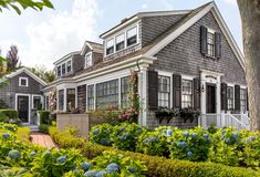 a house that is surrounded by bushes and flowers in the front yard, with blue hydrangeas around it