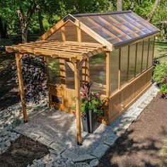 a small wooden structure with a roof and windows in the middle of a garden area